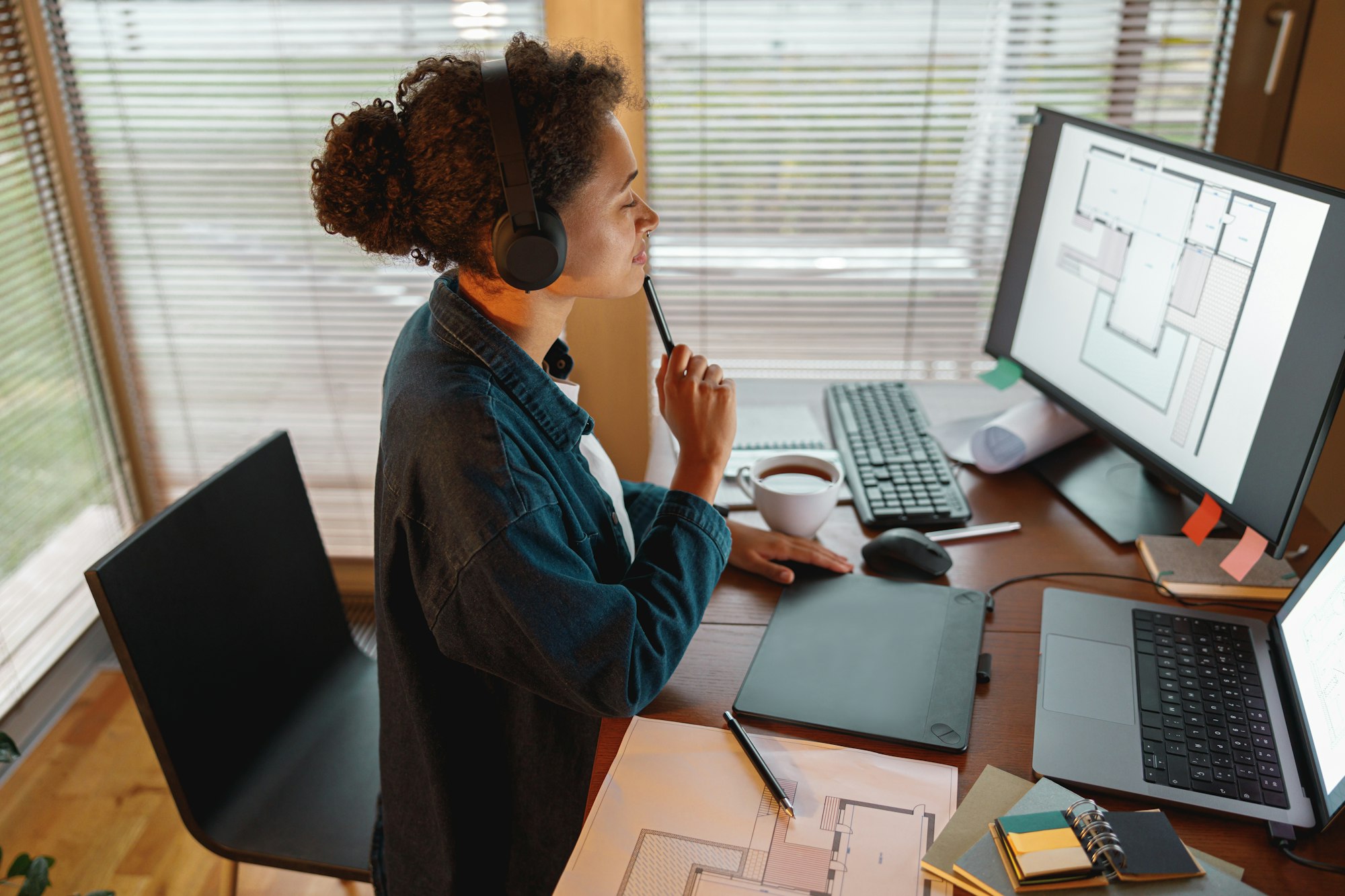 Afro american woman interior designer in headphones works in home office drawing on graphic tablet